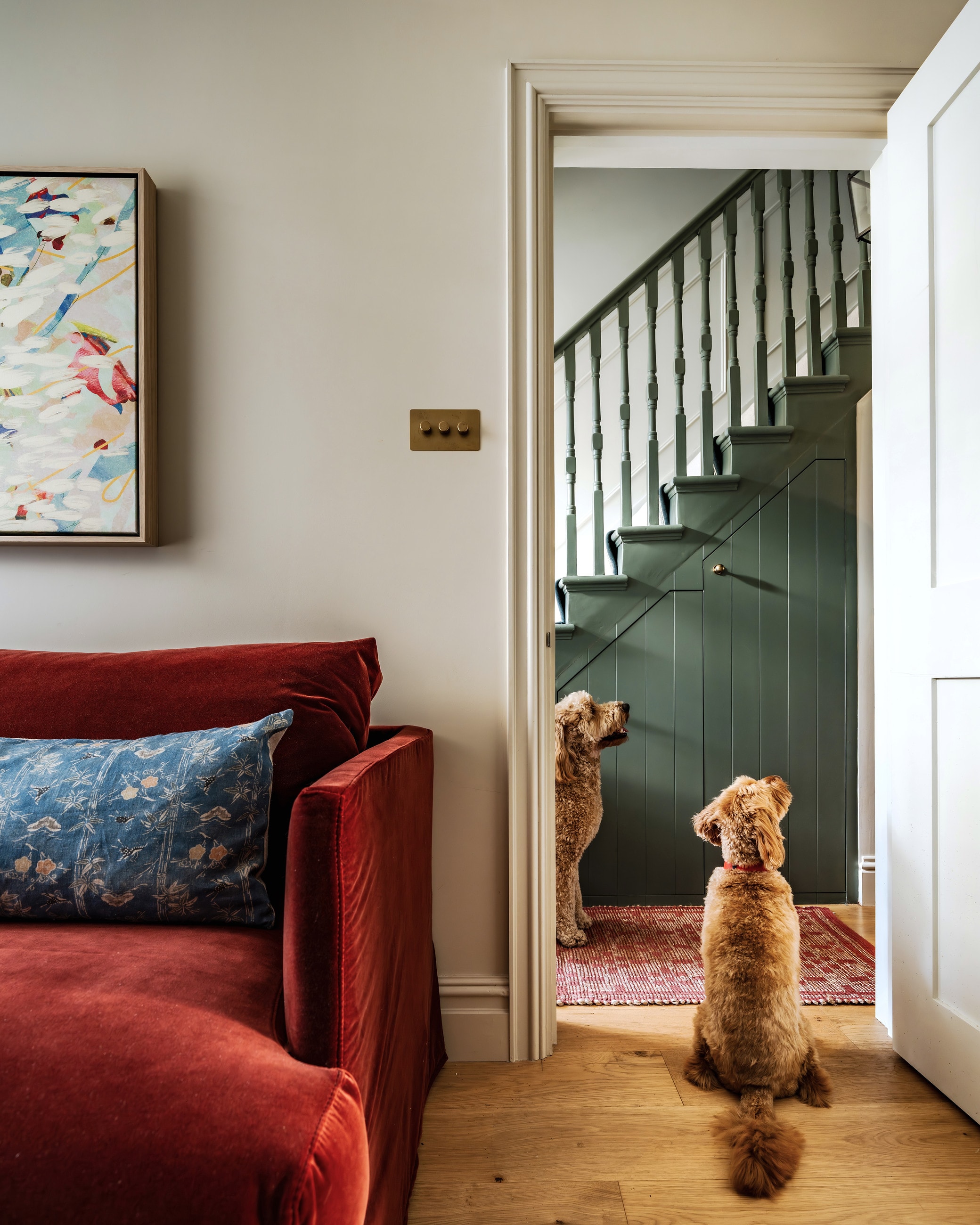 Red velvet sofa by a doorway, with a dog looking out towards a green staircase